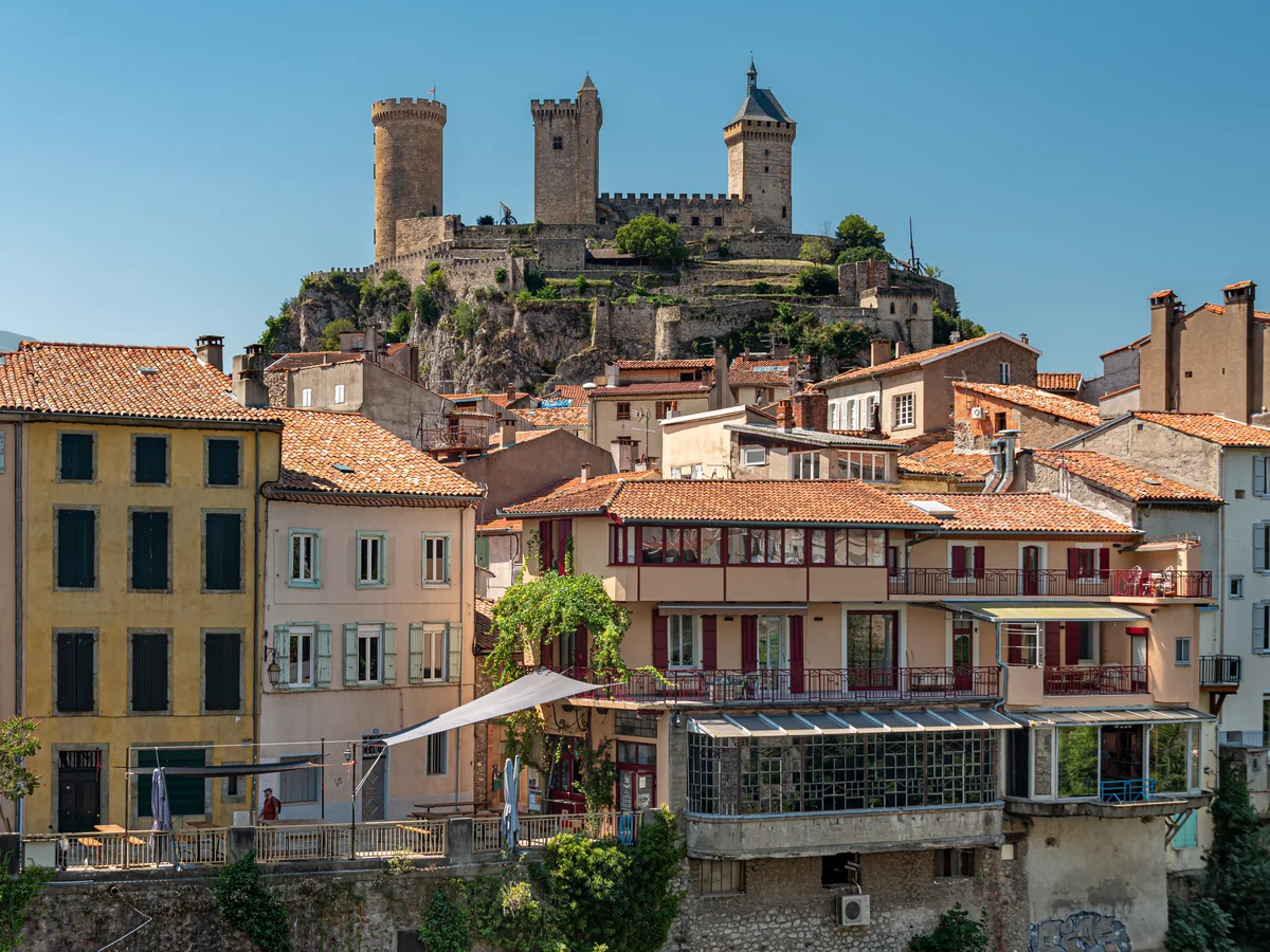 Foix, en Ariège : le château et ses trois tours dominent les toits de tuiles et les façades ocre de la vieille ville.